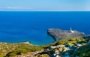 Lighthouse on a small Greek island, with crashing waves against rocky cliffs in the foreground.