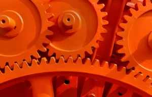 Close-up of a group of orange colored gears, representing the Antikythera Mechanism, a complex ancient astronomical calculator.