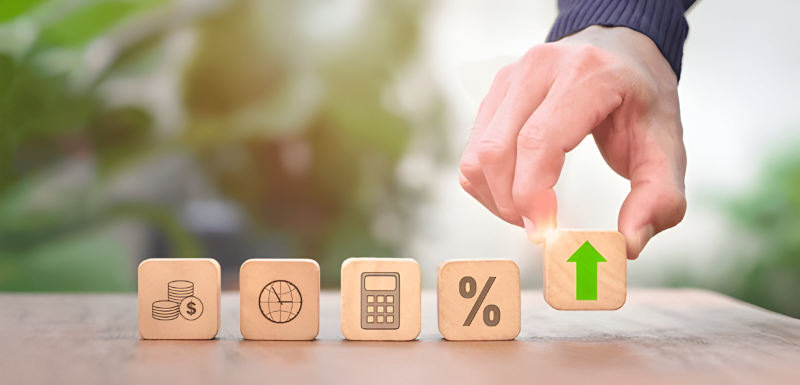 Person arranging wooden blocks with symbols of stacked coins, a globe, a calculator, a percentage sign, and an upward arrow